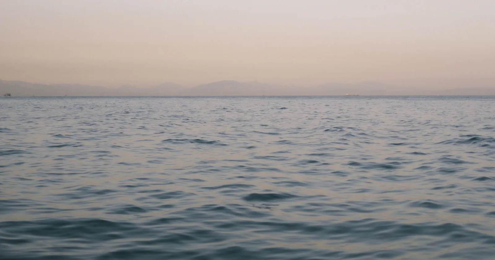 Calm Mediterranean sea at dusk with distant harbour lights